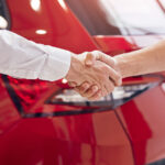 Unrecognizable,Male,Customer,And,Manager,Shaking,Hands,Against,Red,Vehicle