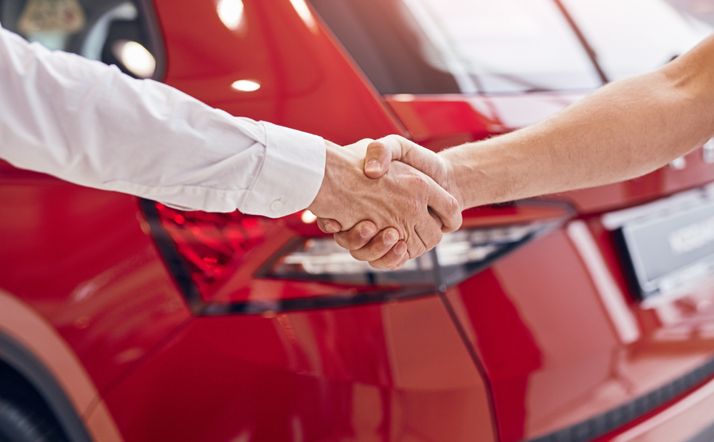 Unrecognizable,Male,Customer,And,Manager,Shaking,Hands,Against,Red,Vehicle