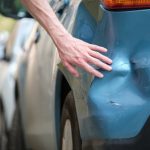 Driver,Hand,Examining,Dented,Car,With,Damaged,Fender,Parked,On